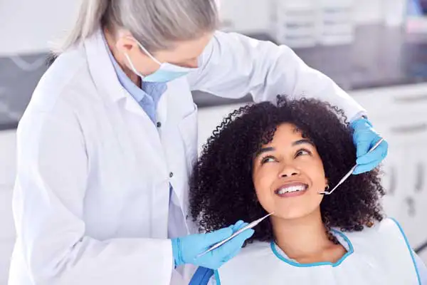 Young woman with black curly and poofy hair looks up and smiles at older female dentist at McHenry Smile Center.