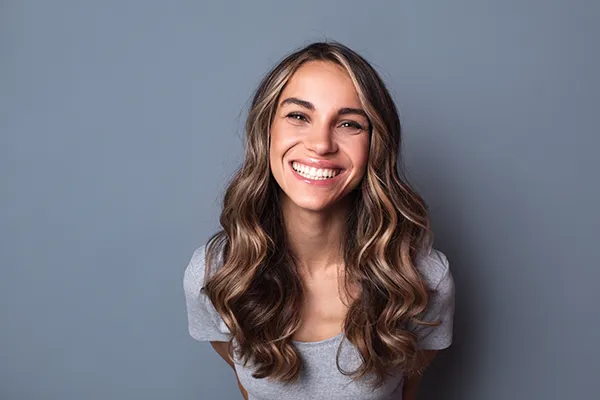 Joyful woman with long and curly brown hair showing off her beautiful teeth with a smile.