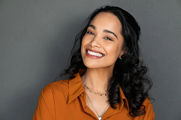 Beautiful woman with black, long, and curly hair showing off her brilliant teeth with a smile, at McHenry Smile Center.