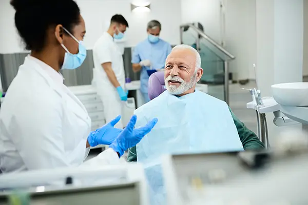 Older man patient sitting in dental chair calmly discussing his oral health with his female dentist, wearing a mask and lab coat, at McHenry Smile Center.