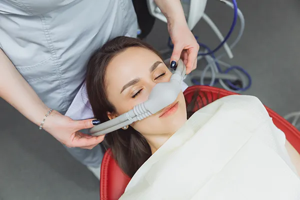 Dental assistant fitting a sedation mask over the nose of her calm female patient, at McHenry Smile Center.