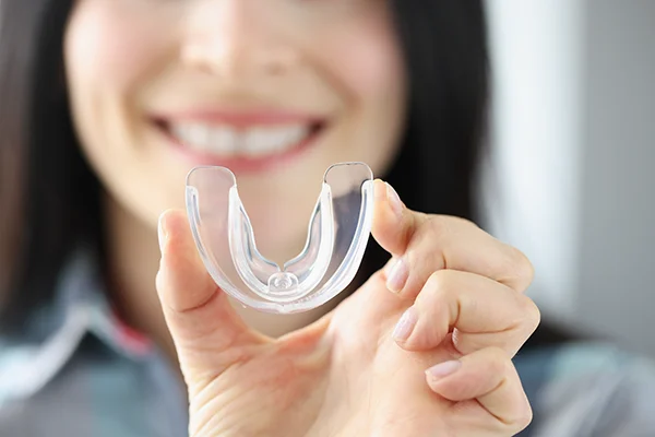 Close up of a simple mouthguard being held up by a smiling woman with long straight black hair, wearing a collared shirt.