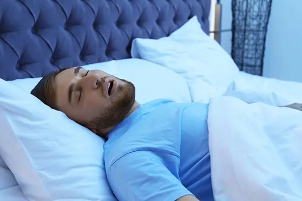 Young man with sleep apnea snoring while trying to sleep in his bed.